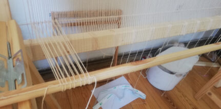 Adding heddles at the heddle rod, a system of looped twine attached to the warp, which will enable to move the threads while weaving. 