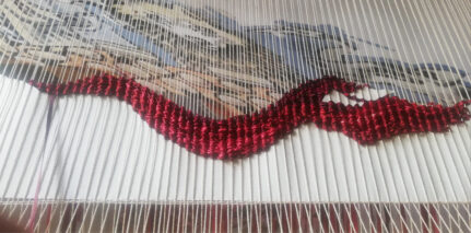 Woven shiny weft yarn and warp yarn with gobelin image in the background
